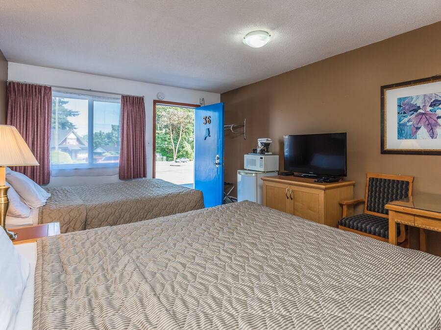 Ett hotellrum med två sängar, en TV, ett skrivbord, en stol, en lampa och en dörr som leder ut.