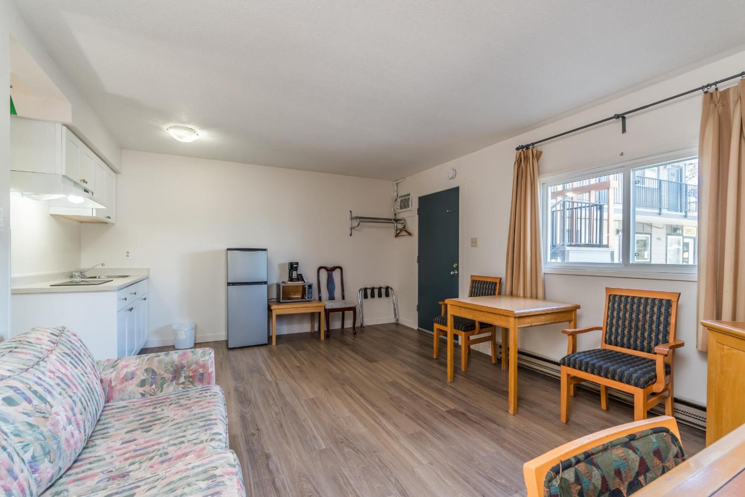 A compact living space with a kitchenette, a sofa, a dining table with chairs, and a window with curtains.
