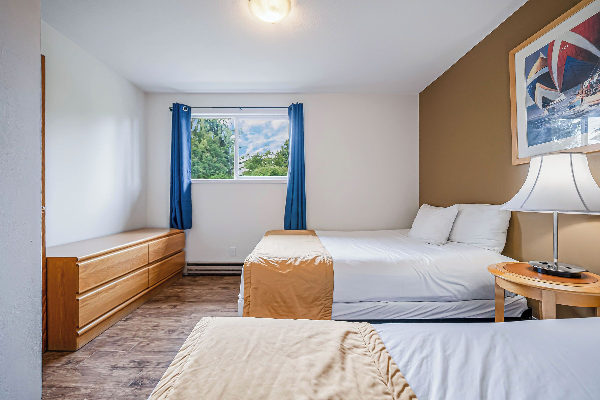 A hotel room with a bed, a bench, a bedside table, and a window with curtains.