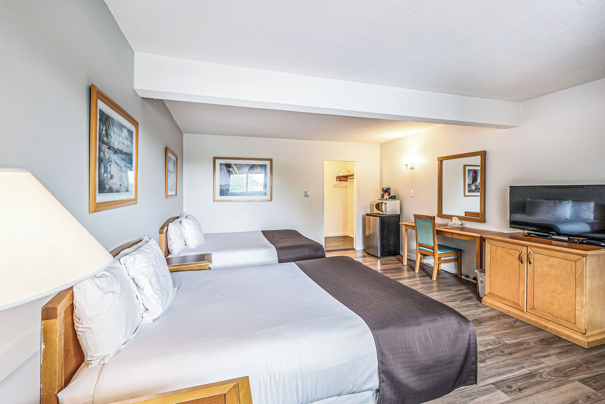 A hotel room with two beds, a desk with a chair, a television, and framed pictures on the walls.