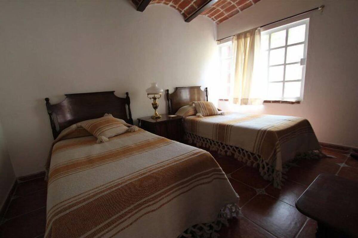 A room with two beds, a nightstand, a lamp, and a window with curtains.