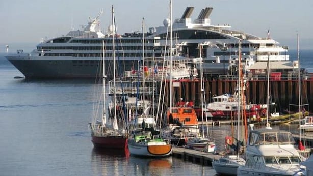 Ein großes Kreuzfahrtschiff liegt in einer Marina, umgeben von mehreren kleineren Booten und Yachten.