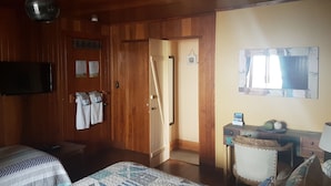 Ein Zimmer mit Holzwänden, einem Bett, einem Schreibtisch mit Lampe, einem Fernseher und einer Tür zu einem anderen Raum.
