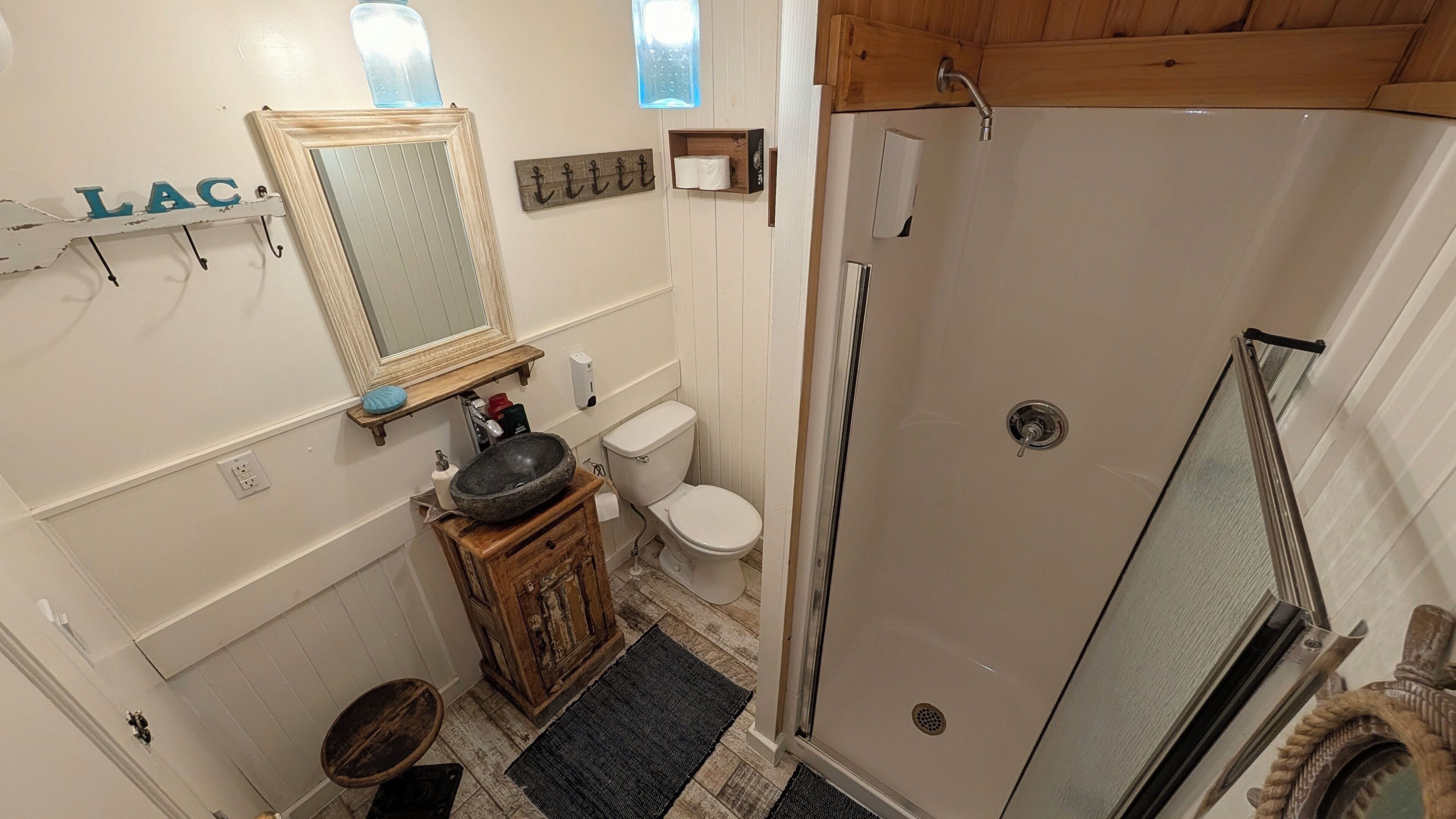 Un baño con tocador de madera, lavamanos, inodoro y ducha con mampara de vidrio.
