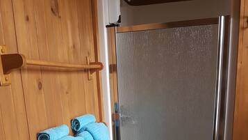 Interior de madera con puerta de vidrio para la ducha y un perchero con dos toallas.