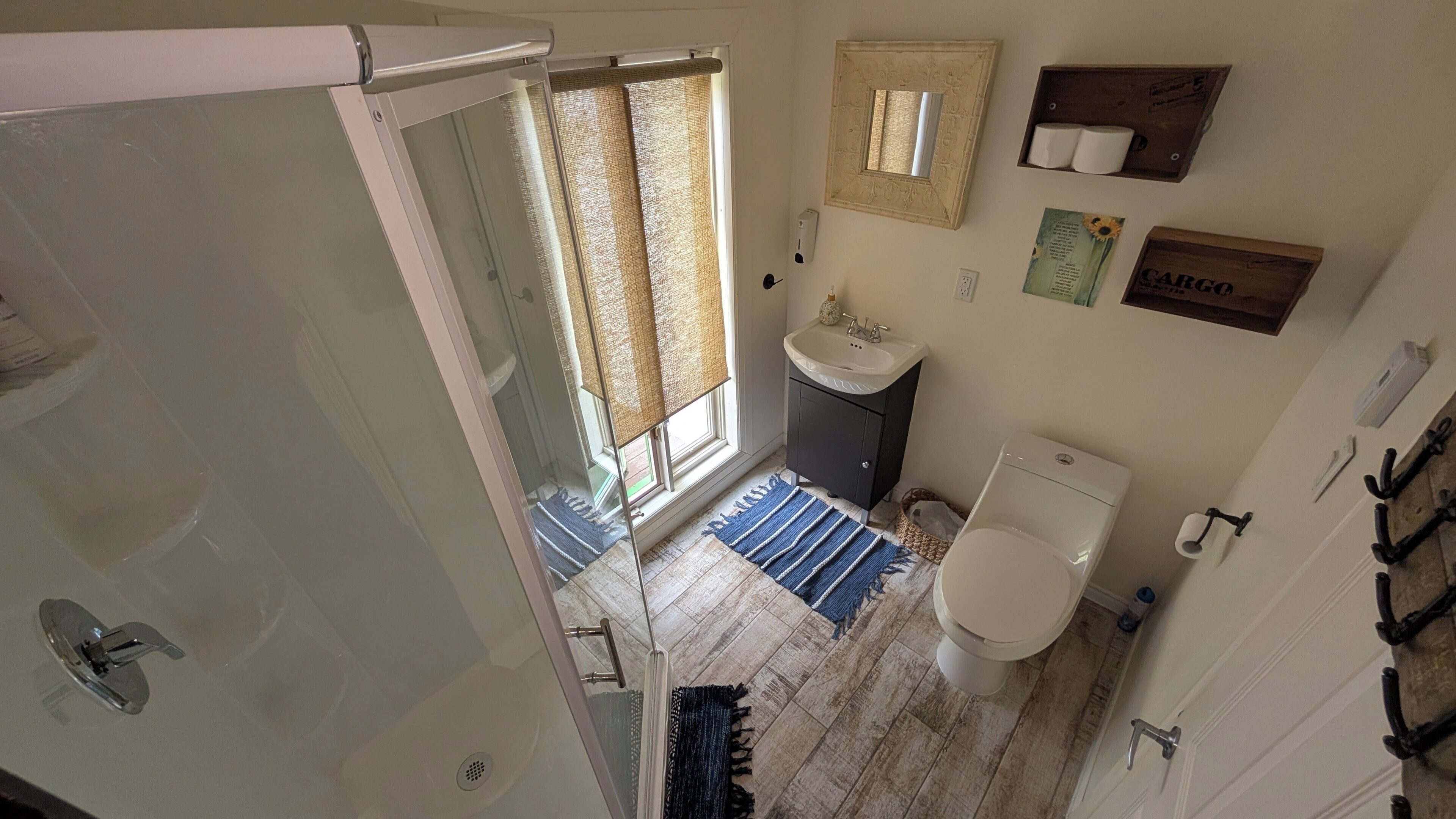 A bathroom with a shower, toilet, sink, and a window with curtains.