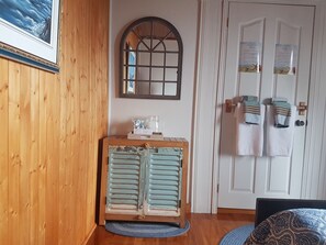 A room with wooden walls, a vintage cabinet, a mirror, and a door with towels and a sign. - Gite au Vieux Pommier (Tadoussac)