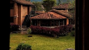 A traditional building with a tiled roof, surrounded by lush greenery and mountains in the background. - Lizzy Wasi Urubamba (Urubamba)
