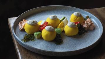 A plate of food with various items including yellow spherical objects topped with a white substance, green and red vegetables, and a dollop of pinkish substance.