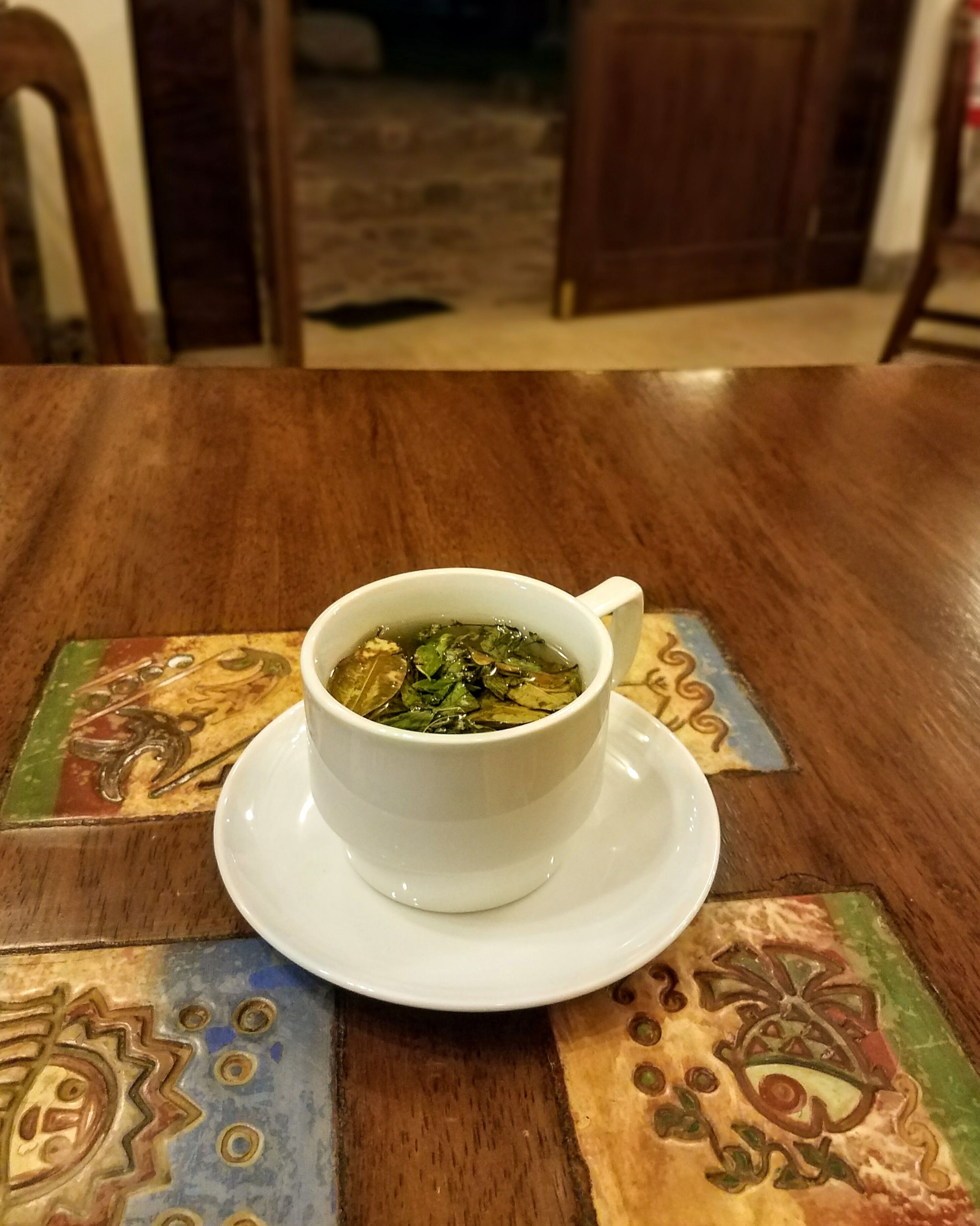 Eine weiße Teetasse auf einem Holztisch mit Untersetzer.