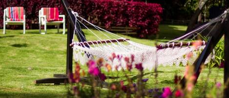 A hammock in a garden with a chair and a table in the background.