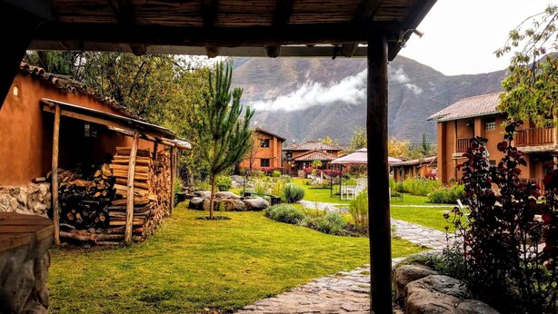 A rustic lodge with stone walls, a wooden deck, and a well-maintained garden with a stone pathway. - Lizzy Wasi Urubamba (Urubamba)