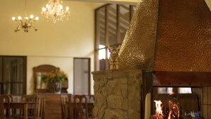 A stone fireplace with a decorative hood, a dining area with wooden furniture, and a chandelier. - Lizzy Wasi Urubamba (Urubamba)