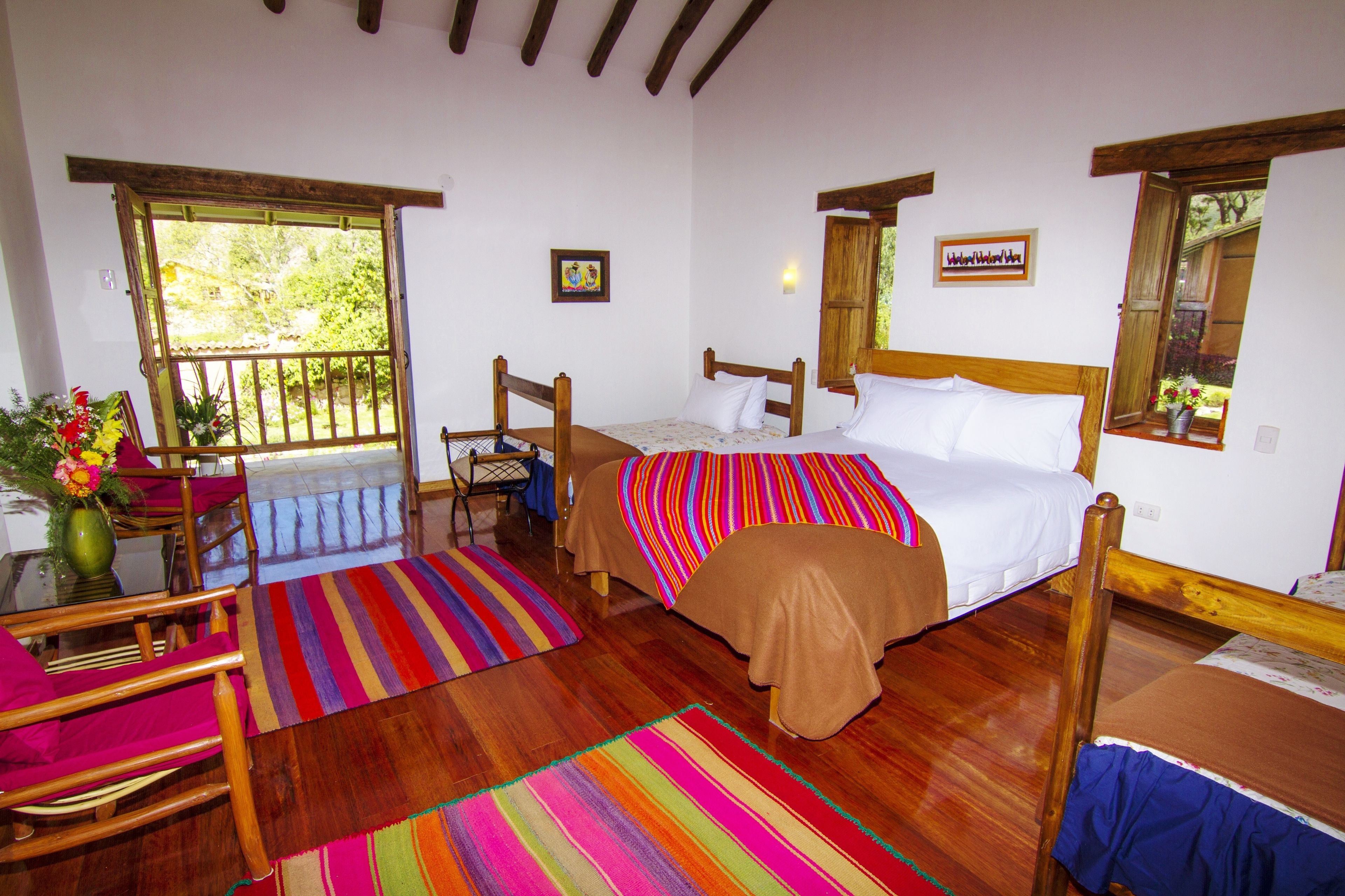 A bedroom with a wooden bed, a colorful striped rug, a wooden chair, and a window with a view of greenery.