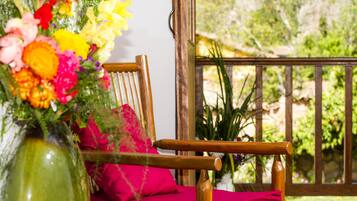 A wooden chair with a red cushion, a green vase with flowers, and a wooden railing.