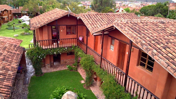 A traditional building with a tiled roof, a balcony with a railing, and a small courtyard with a lawn and plants.