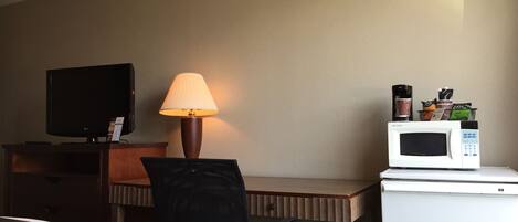 A hotel room with a bed, a desk, a television, a lamp, a microwave, and a coffee maker.