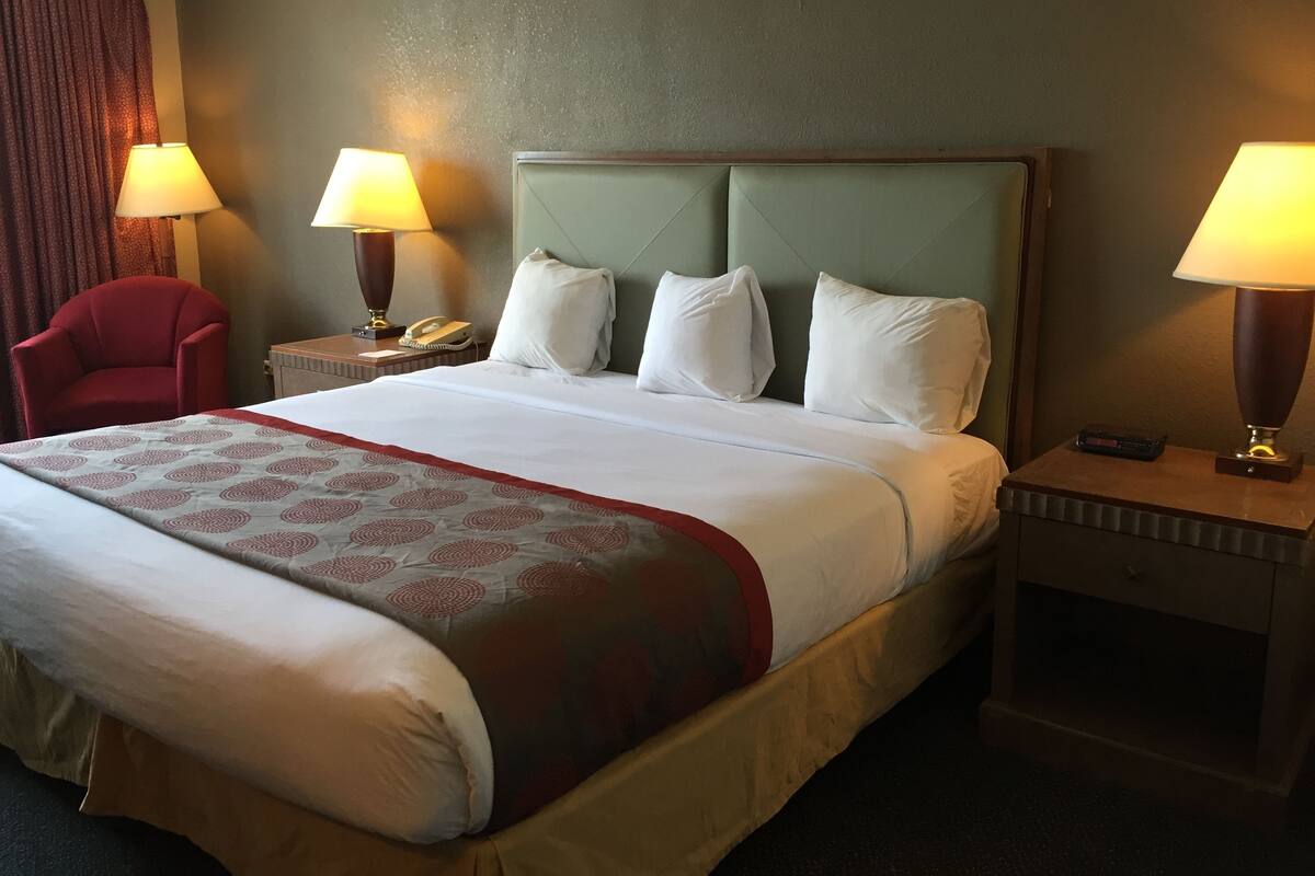 A hotel room with a large bed, two bedside tables, a red armchair, and two lamps.