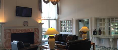 A spacious living room with a fireplace, leather sofas, a coffee table, and a chandelier.