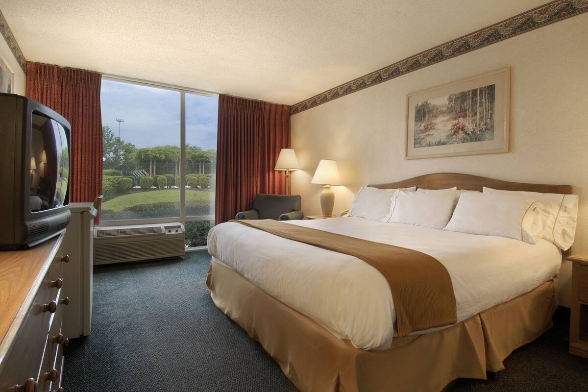 A hotel room with a large bed, a TV, a desk, and a window with curtains.