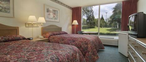 A hotel room with two beds, a television, a desk, and a window with a view of the outdoors.