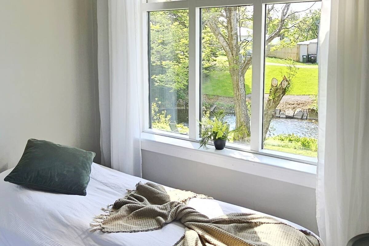 A bedroom with a bed, a window with curtains, and a view of greenery outside.
