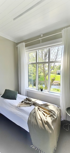 A bedroom with a bed, a window with curtains, and a view of greenery outside. - Árból Guesthouse (Husavik)