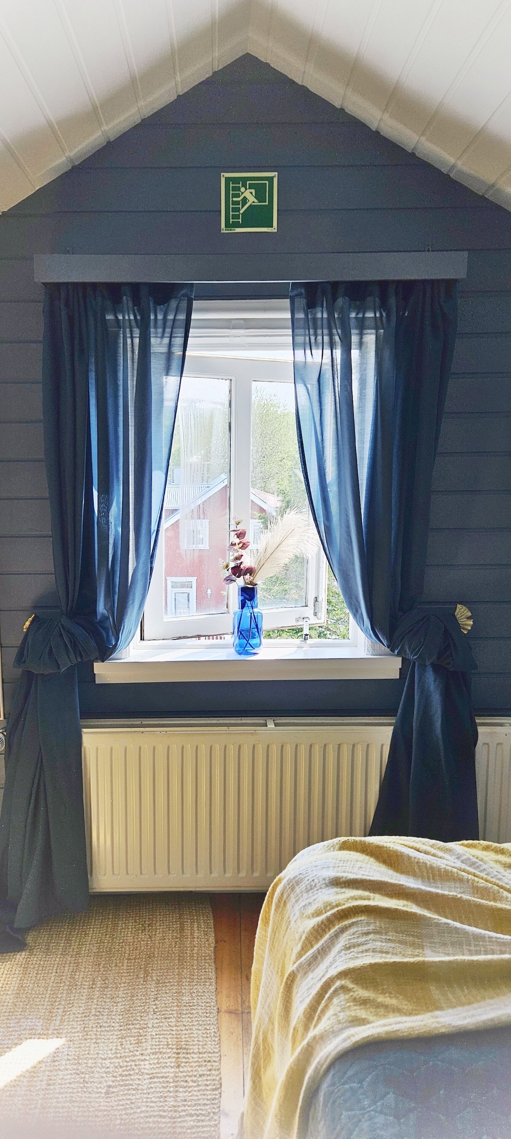 Une chambre avec une fenêtre, des rideaux, un radiateur et un lit.