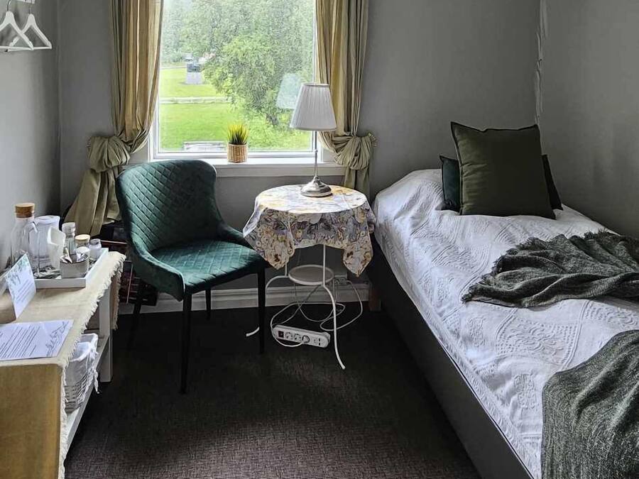 A bedroom with a bed, a desk, a chair, a lamp, and a window with curtains.