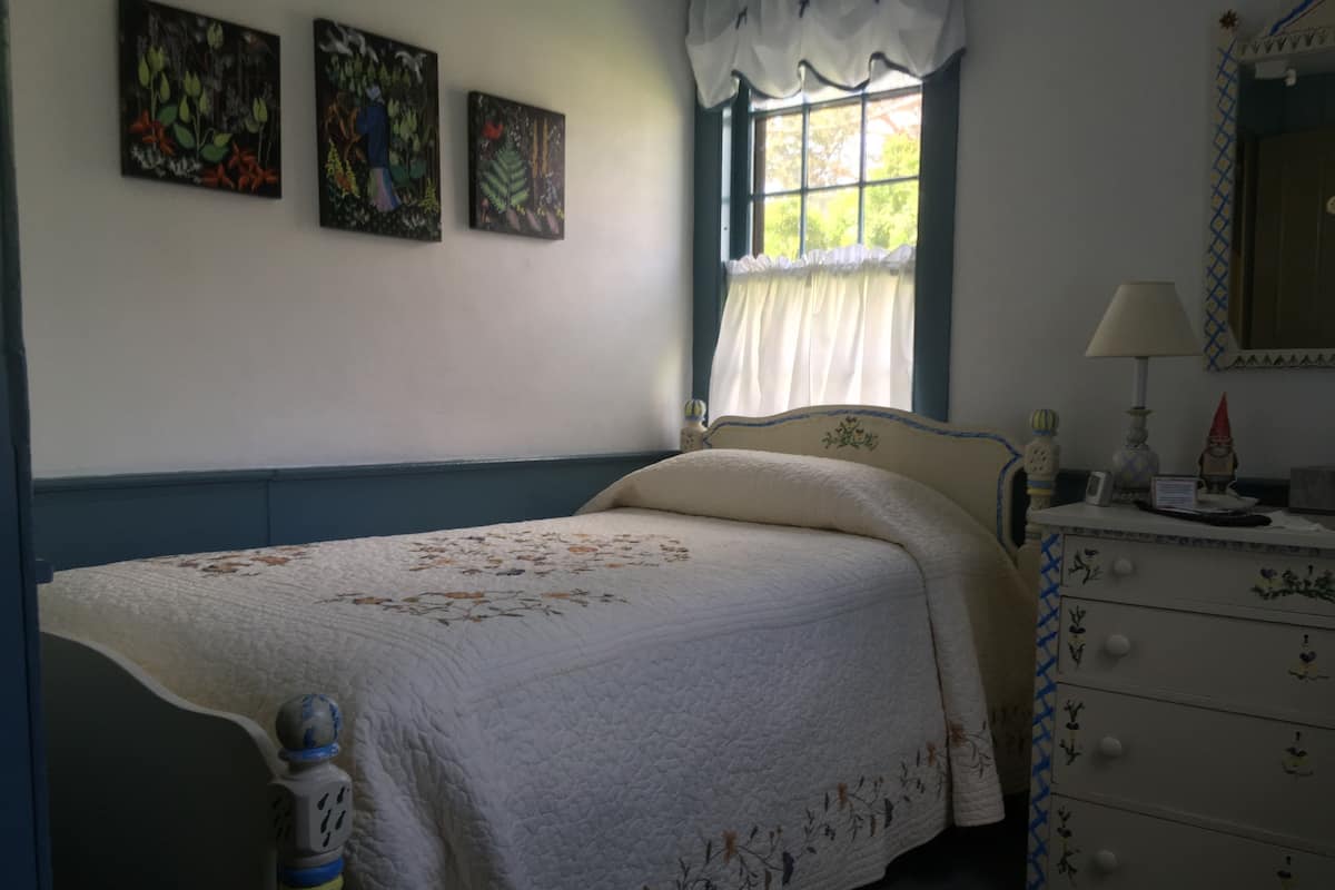 A bedroom with a bed, a dresser, a window with curtains, and three paintings on the wall.