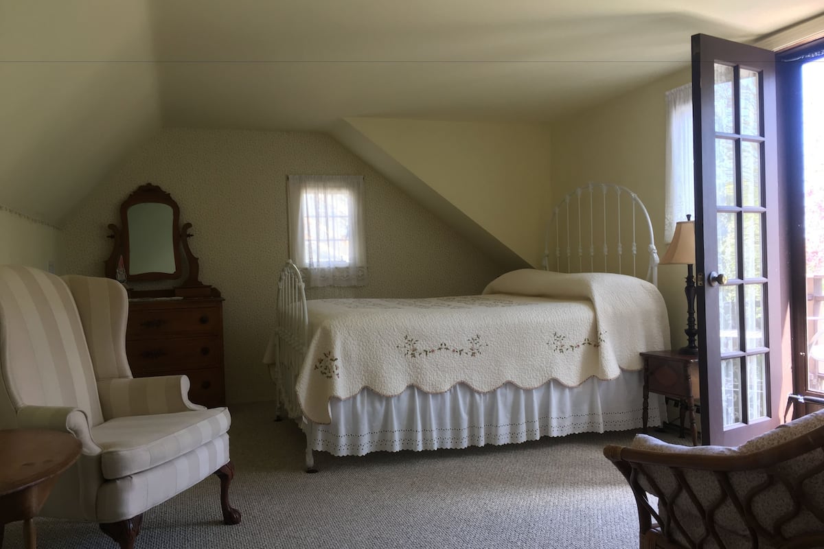 A bedroom with a bed, a chair, a dresser, a mirror, and a window.