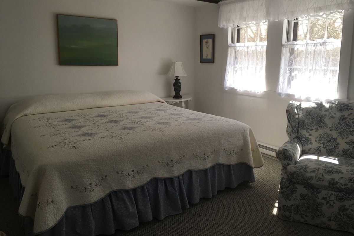A bedroom with a bed, a chair, a lamp, and a painting on the wall.