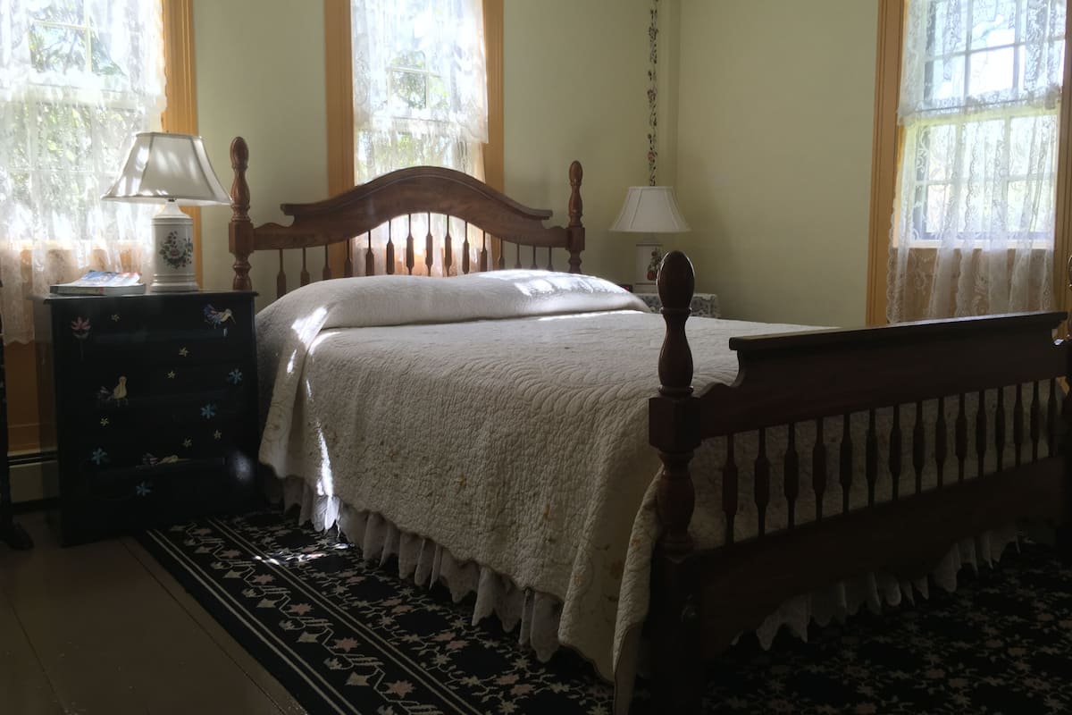 A bedroom with a wooden bed, a nightstand, a lamp, and a window with curtains.