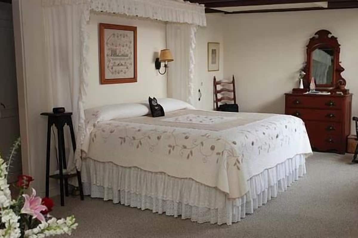 A bedroom with a four-poster bed, a nightstand, a dresser, and a mirror.