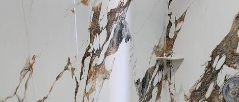 A bathroom with a marble wall and a white bathtub.