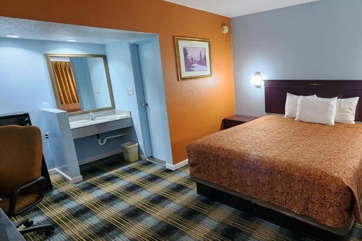A hotel room with a bed, a desk with a chair, a vanity with a mirror, and a nightstand.
