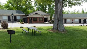 A building with a brick facade and a large tree in front. There are picnic tables and a trash bin in the foreground. - Kentucky Lake Inn (Gilbertsville)