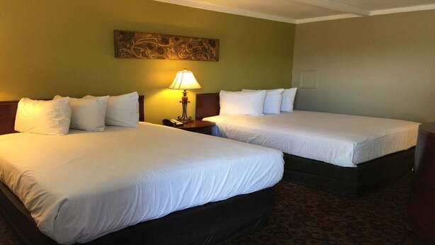 A hotel room with two beds, a nightstand with a lamp, and a decorative wall piece. - Kentucky Lake Inn (Gilbertsville)