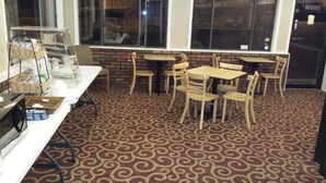 A restaurant interior with patterned carpet, wooden tables and chairs, and a counter with baskets and a coffee machine. - Kentucky Lake Inn (Gilbertsville)