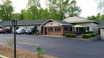 A motel with a single-story brick building, a covered parking area, and a small lawn area with trimmed bushes.