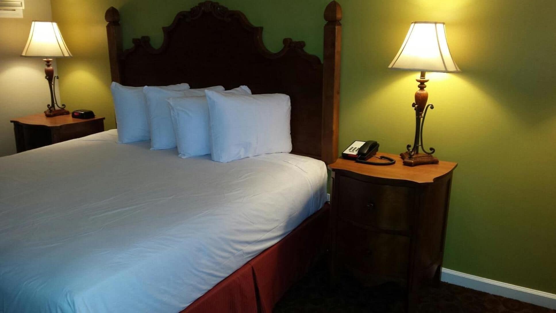 A neatly made bed with white linens and pillows, flanked by two bedside tables with lamps and a telephone.