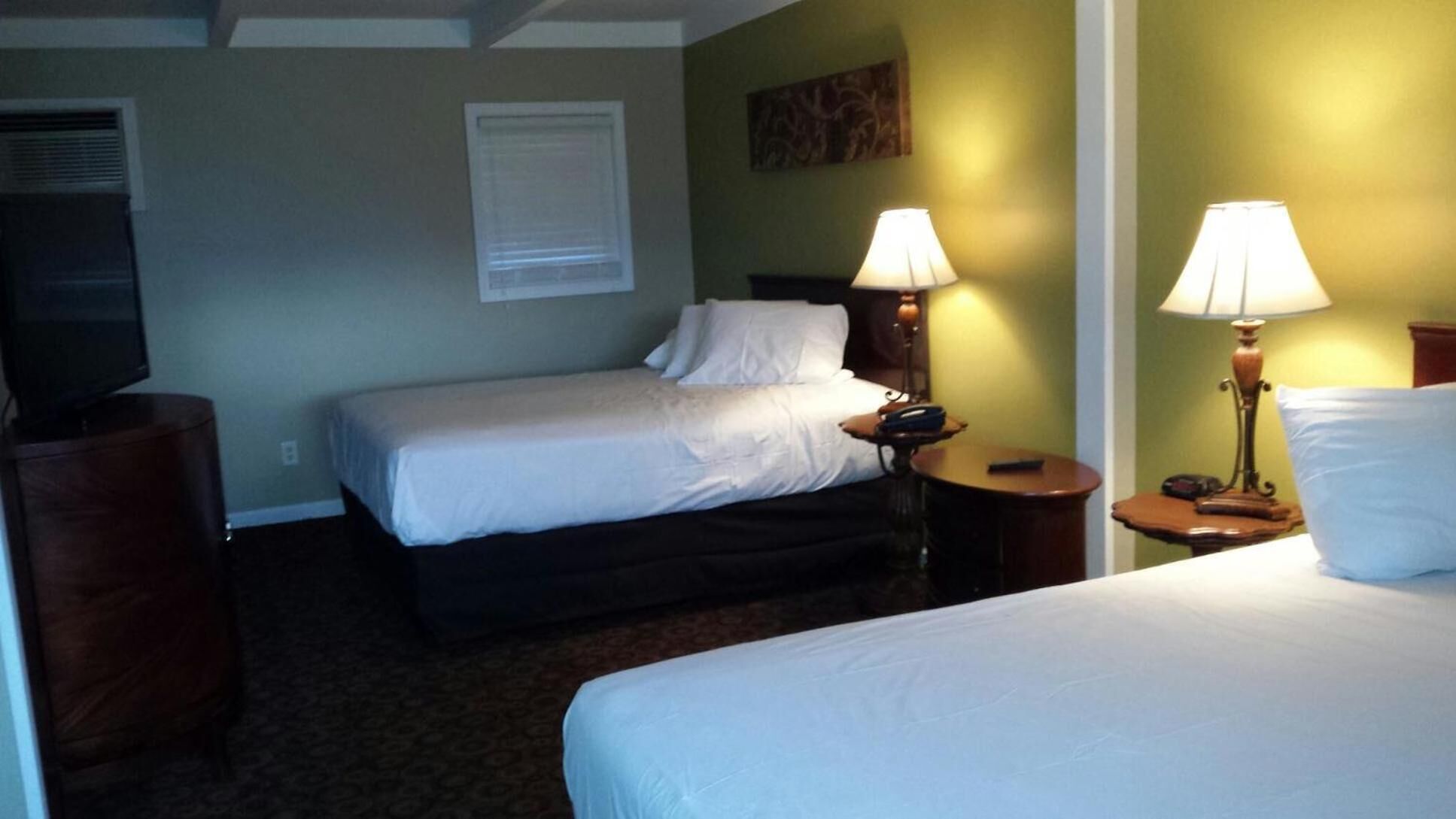 A hotel room with two beds, a television, a lamp, and a painting on the wall.