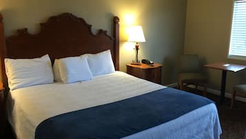 A neatly made bed with white and blue bedding, a wooden headboard, a bedside lamp, a chair, and a small table.