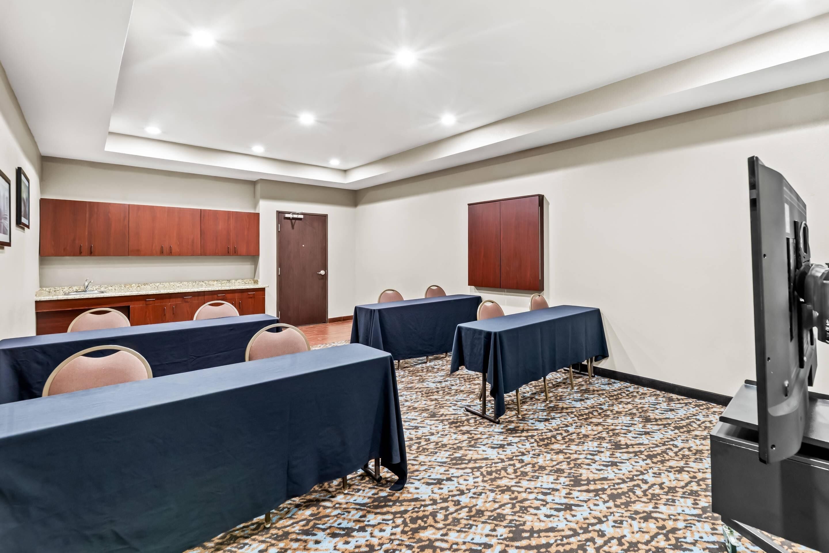 Un salón de conferencias con mesas, sillas, un televisor y una alfombra estampada.