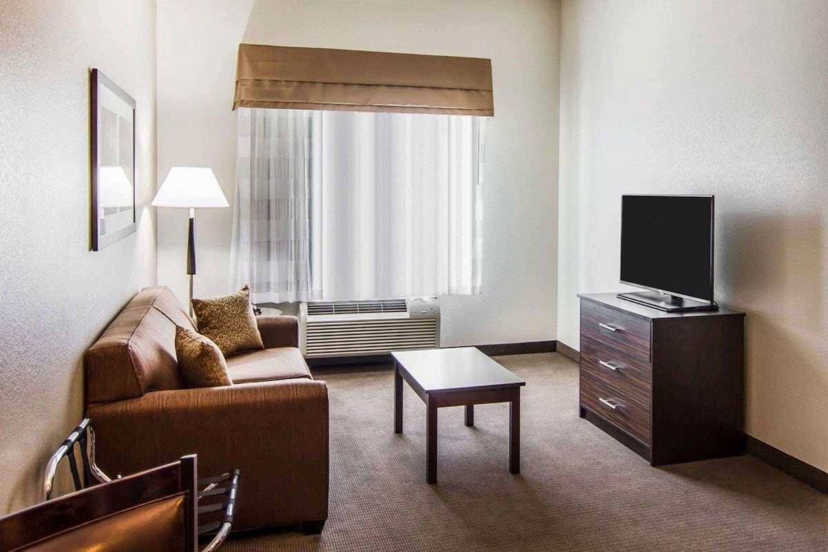 A hotel room with a sofa, a TV on a cabinet, a lamp, and a window with curtains.