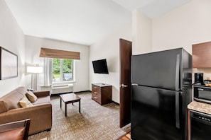 A compact hotel room with a kitchenette, a sofa, a TV, and a window with a view of greenery. - MainStay Suites Lufkin (Lufkin)