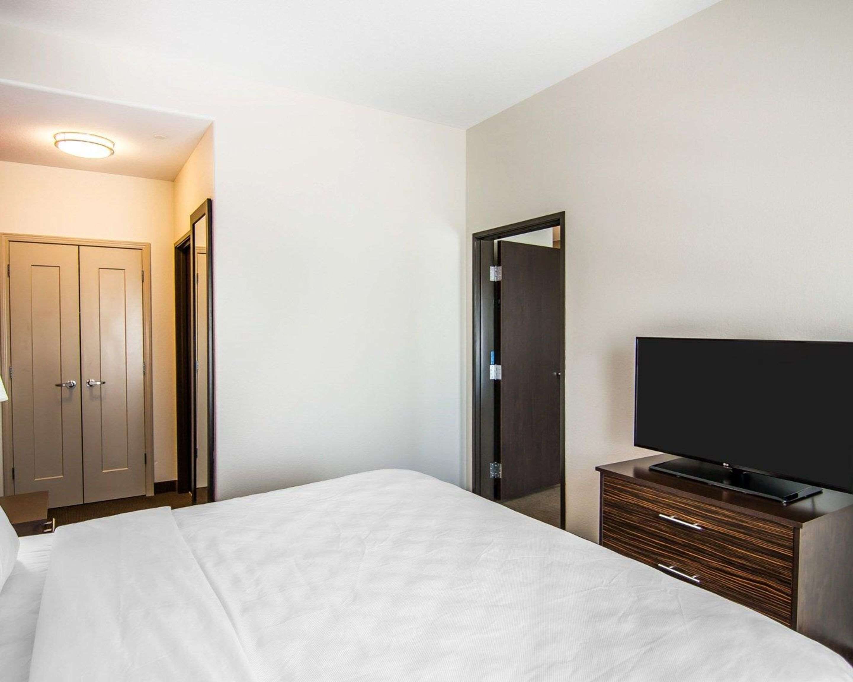 Una habitación de hotel con una cama, un televisor sobre un tocador de madera y una puerta con espejo.