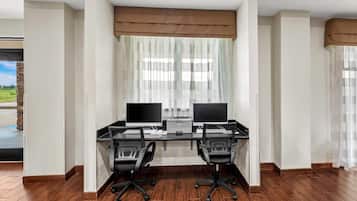 A modern office space with two desks, two chairs, and a large window with sheer curtains.