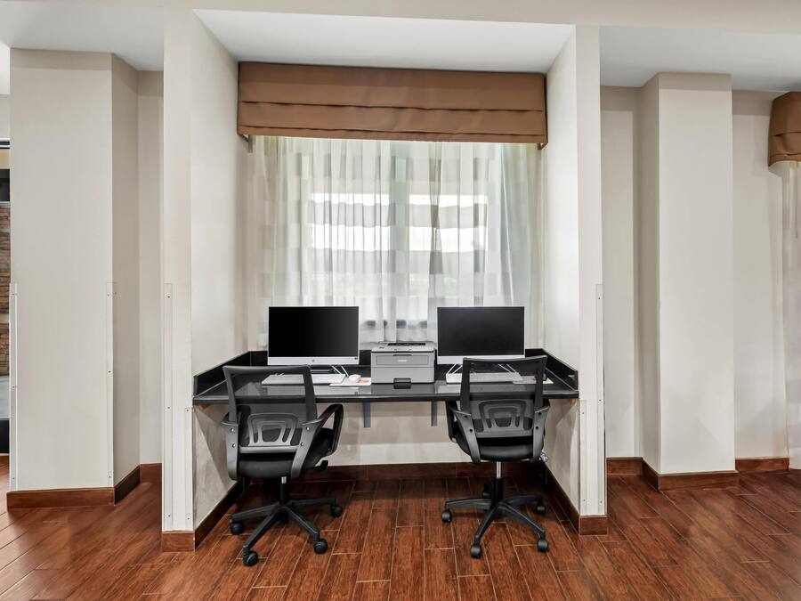 A modern office space with two desks, two chairs, and a large window with sheer curtains.