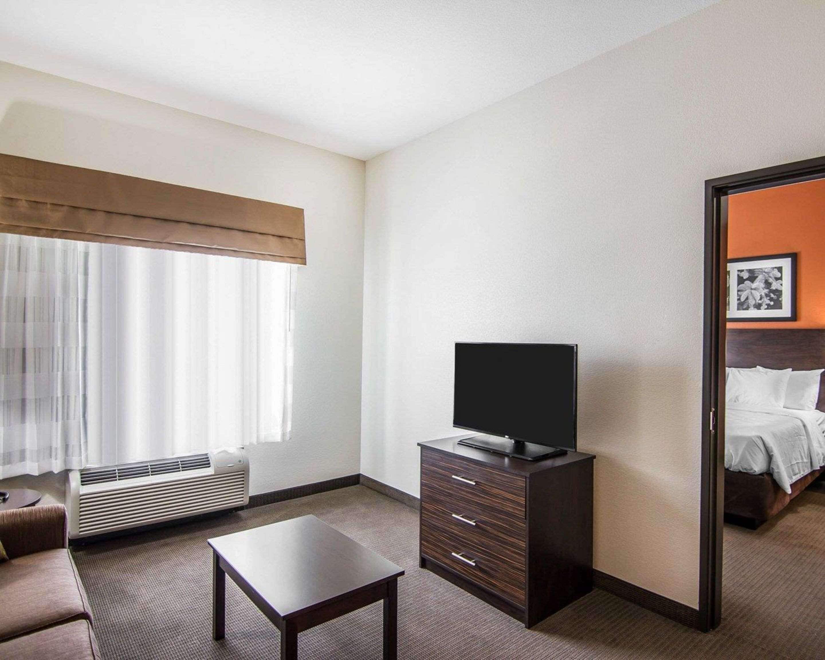 Una habitación de hotel con una cama, un televisor en una cómoda, una mesita y una ventana con cortinas.
